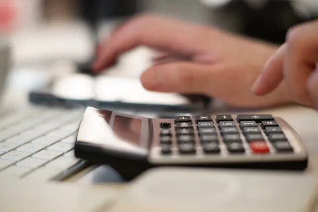 Close-up of hands using a calculator and keyboard in a financial setting, indoors. Comptabilité PME : tenir une comptabilité conforme au droit suisse